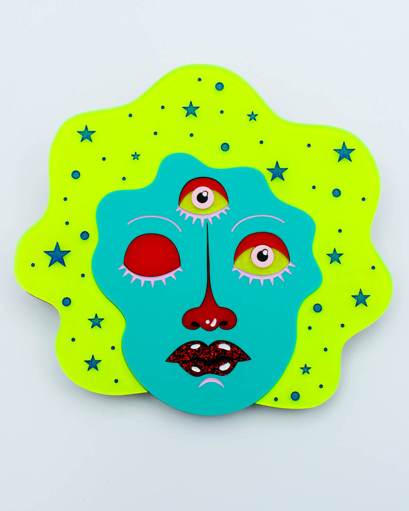Colorful wall art of a three-eyed fortune teller face with teal skin, neon yellow hair, and glitter red lips surrounded by stars, art by Electric Cat.