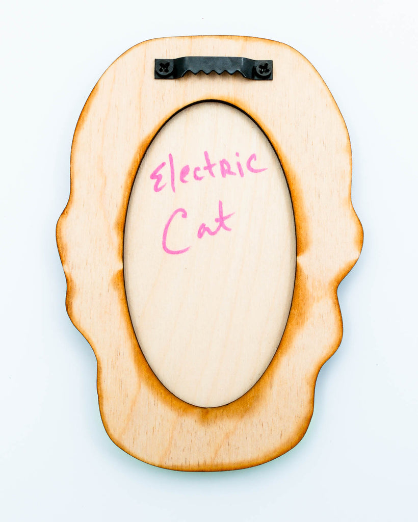 Wood back of the wall art of a surreal green six-eyed woman with black glitter hair and red glitter lips, art by Electric Cat.