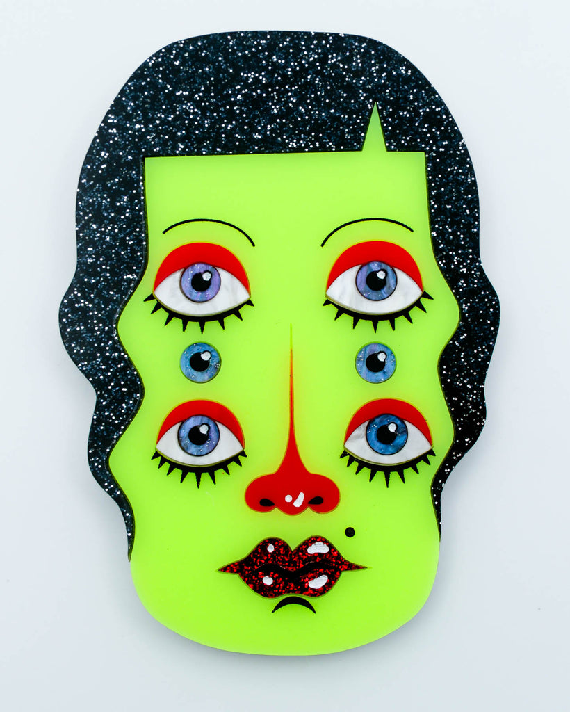 Wall art of a surreal green six-eyed woman with black glitter hair and red glitter lips, art by Electric Cat.