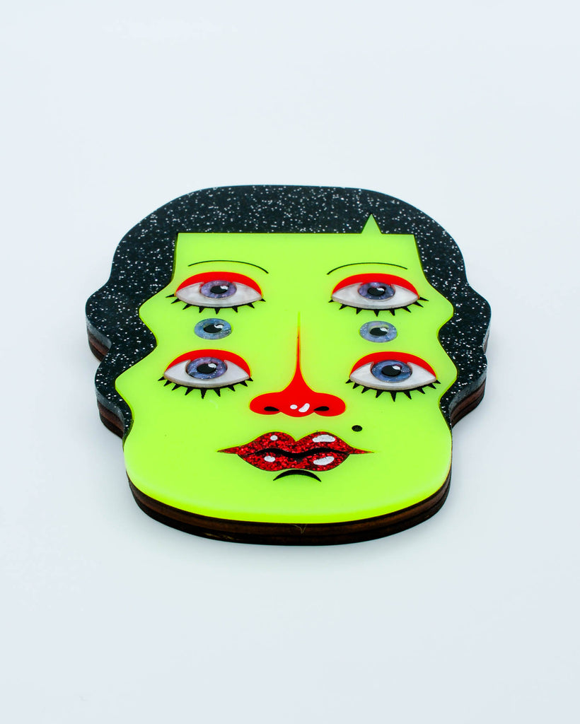 Wall art of a surreal green six-eyed woman with black glitter hair and red glitter lips, art by Electric Cat.