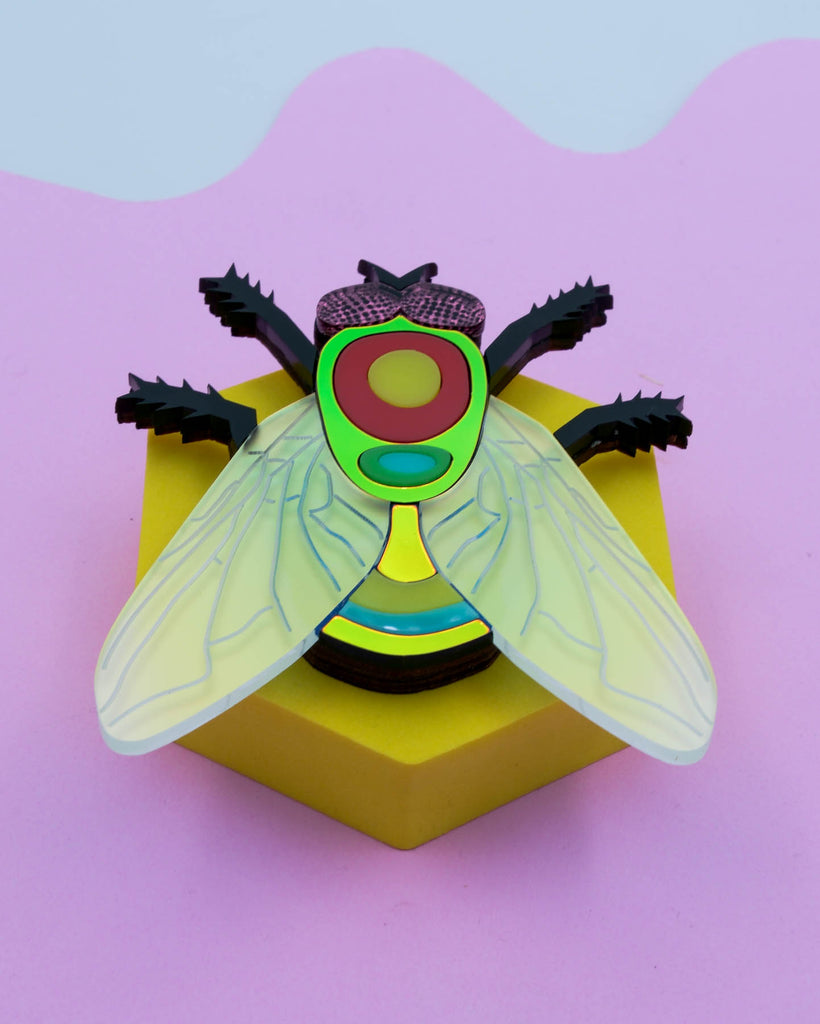 Handmade acrylic fly art piece featuring iridescent wings, black legs, and layered colorful body with pink mirrored eyes, crafted by Electric Cat.