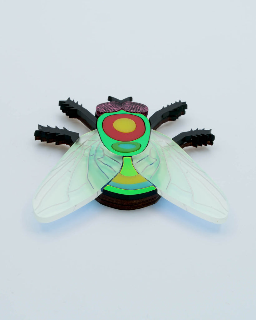 Handmade acrylic fly art piece featuring iridescent wings, black legs, and layered colorful body with pink mirrored eyes, crafted by Electric Cat.