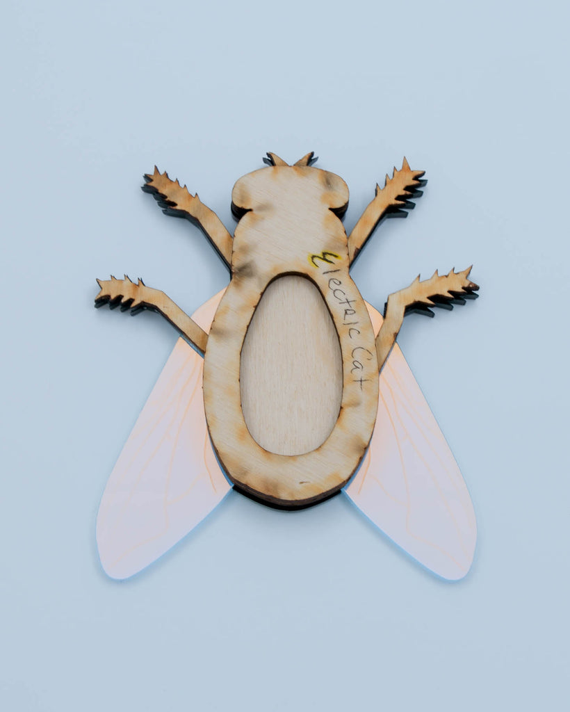 Handmade acrylic fly art piece featuring iridescent wings, black legs, and layered colorful body with pink mirrored eyes, crafted by Electric Cat.