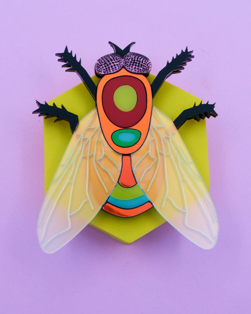 Handmade acrylic fly art piece featuring iridescent wings, black legs, and layered colorful body with pink mirrored eyes, crafted by Electric Cat.