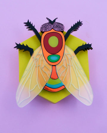 Handmade acrylic fly art piece featuring iridescent wings, black legs, and layered colorful body with pink mirrored eyes, crafted by Electric Cat.