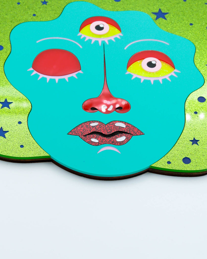 Colorful pop surrealism wall art featuring a teal three-eyed face with one eye closed and sparkling green background, art by Electric Cat.
