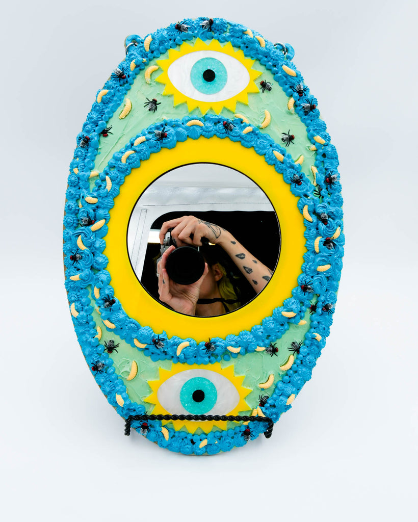 Surreal handmade mirror with textured faux frosting, two glitter eyes, flies, and maggots on blue and yellow frame, art by Electric Cat.