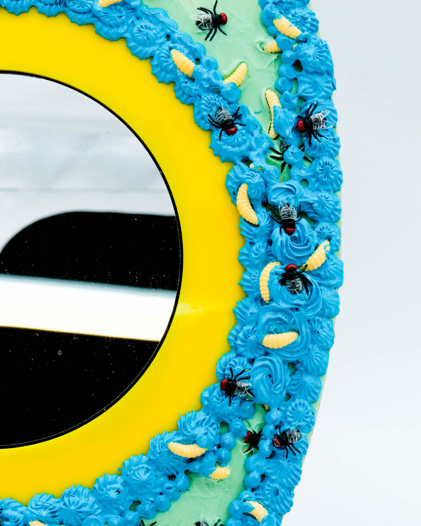 Surreal handmade mirror with textured faux frosting, two glitter eyes, flies, and maggots on blue and yellow frame, art by Electric Cat.