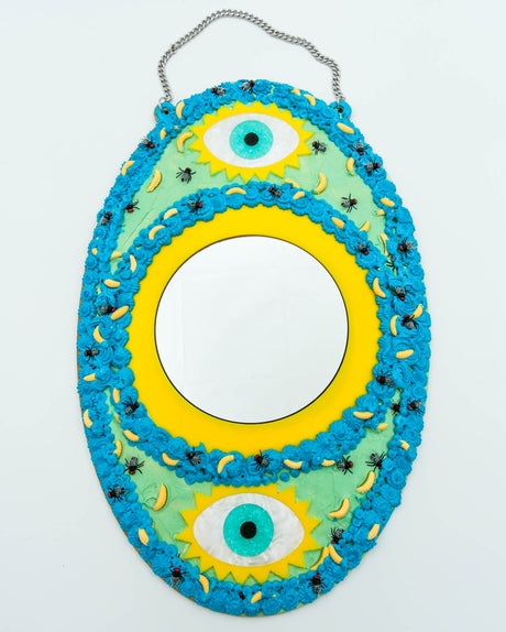 Surreal handmade mirror with textured faux frosting, two glitter eyes, flies, and maggots on blue and yellow frame, art by Electric Cat.