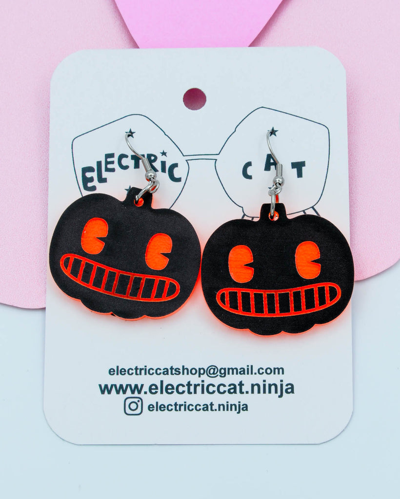 Black pumpkin-shaped earrings with orange details on a white card with branding information.