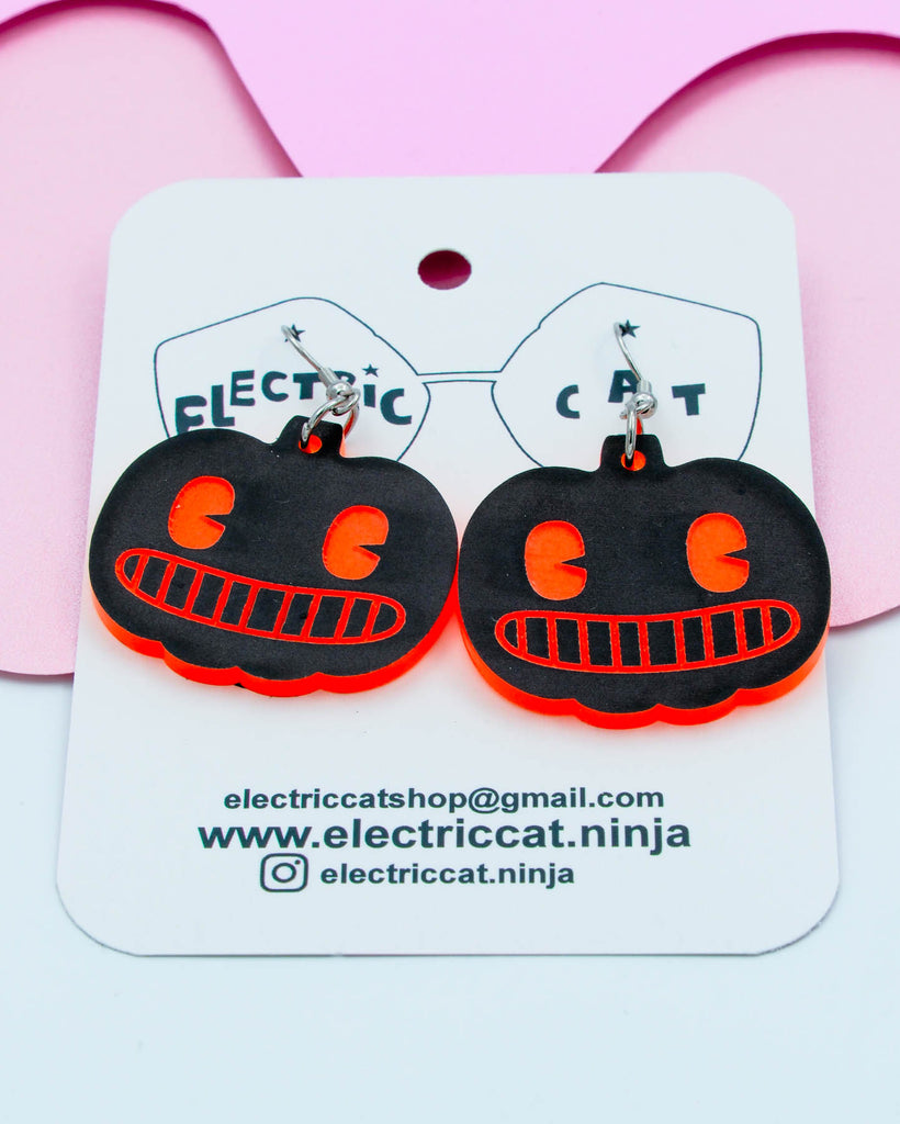 Black and orange pumpkin-shaped earrings on a white card with branding information.