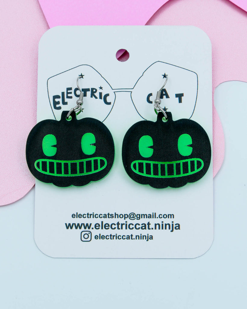 Black and green pumpkin-shaped earrings on a branded card with contact information.