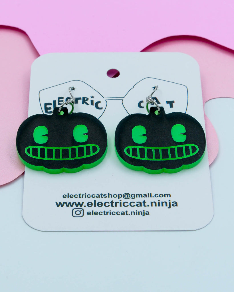 Black and green pumpkin earrings on 'Electric Cat' branded card with pink background