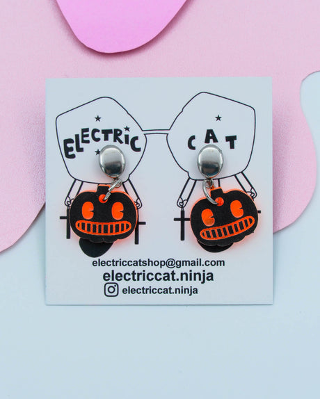Pumpkin-shaped earrings on a card with branding details against a pink background