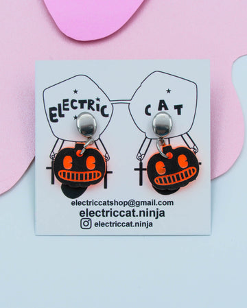 Pumpkin-shaped earrings on a card with branding details against a pink background