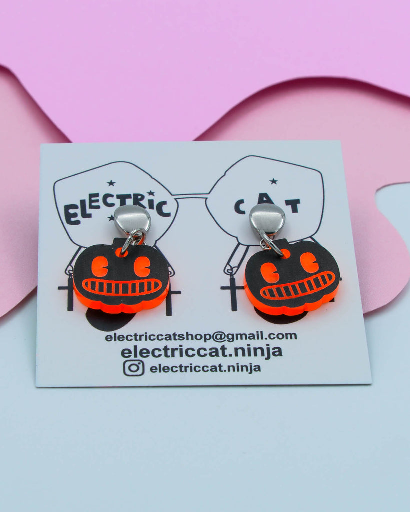 Pumpkin-shaped earrings on a branded card with contact information.