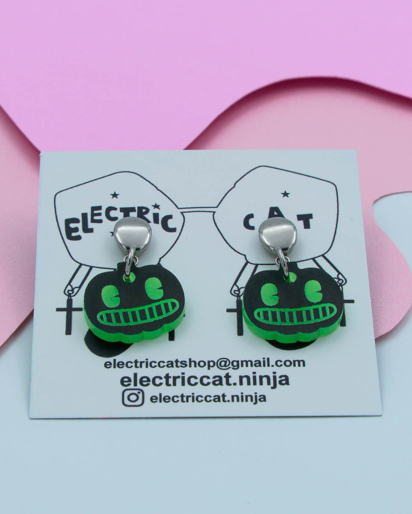 Pair of green and black pumpkin earrings on a branded card with contact information.