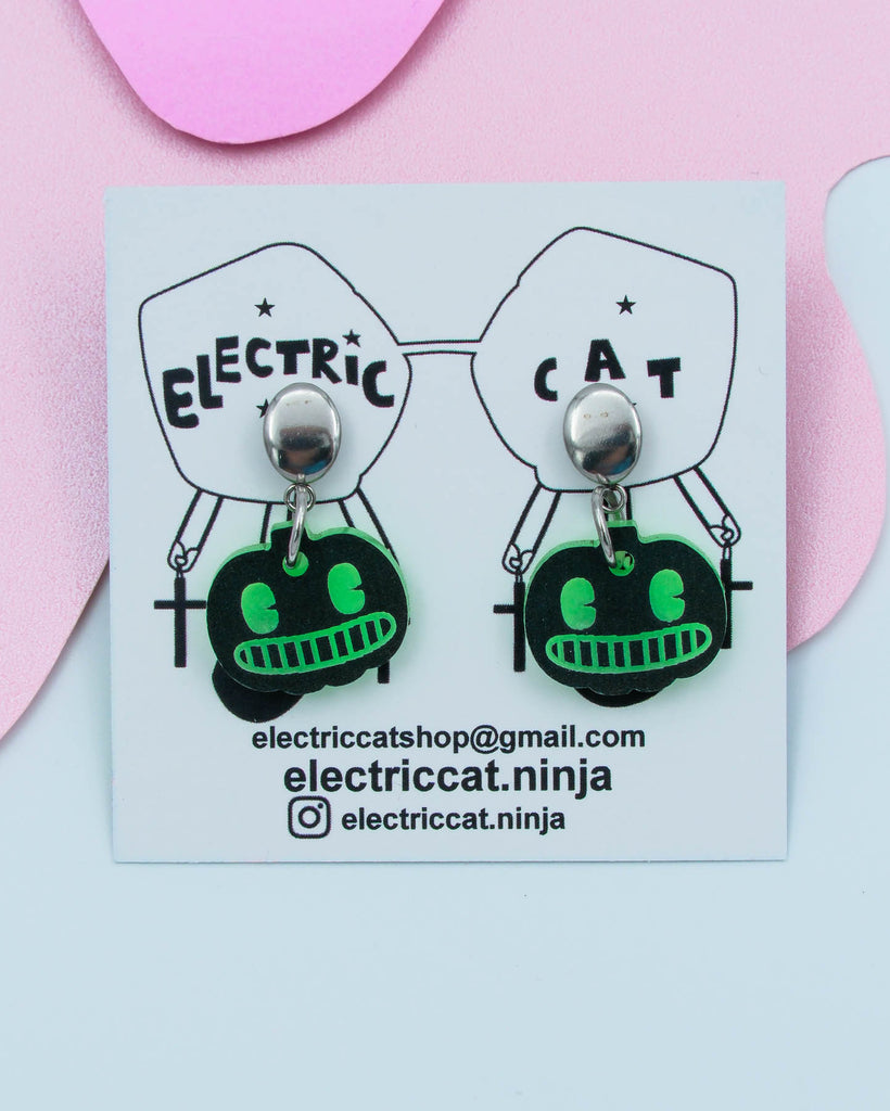 Pair of black and green pumpkin-shaped earrings on a branded card with contact information.