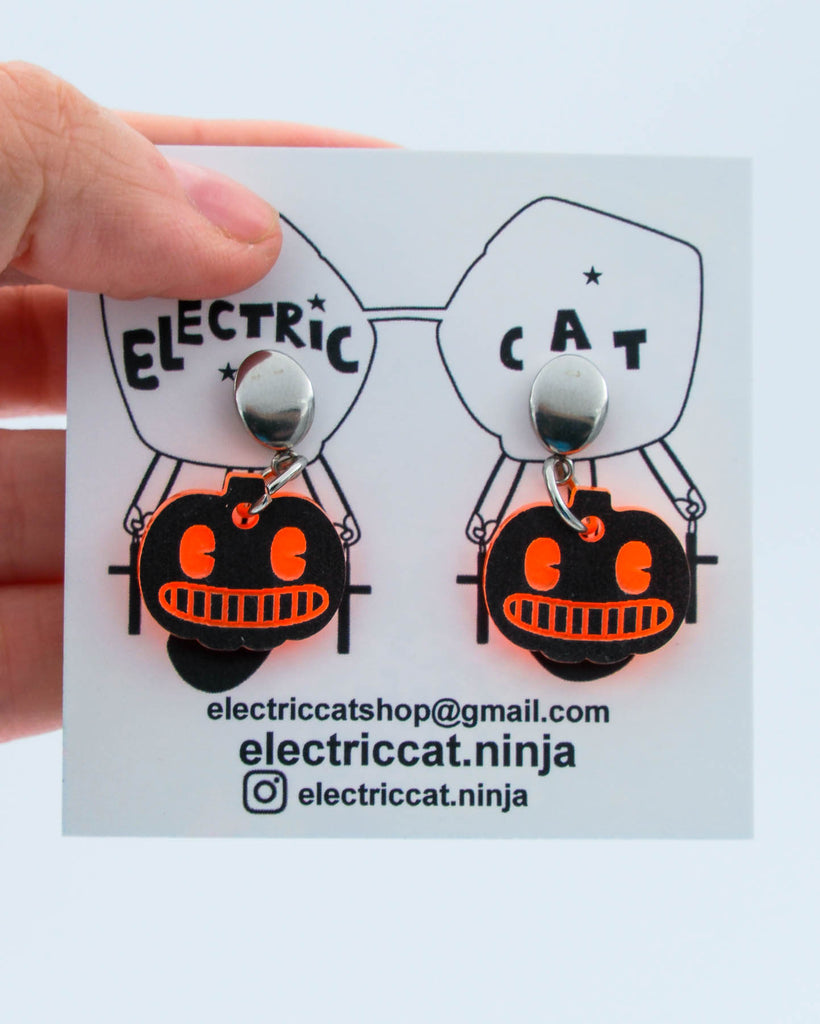 Halloween-themed pumpkin earrings on a branded card with contact information.