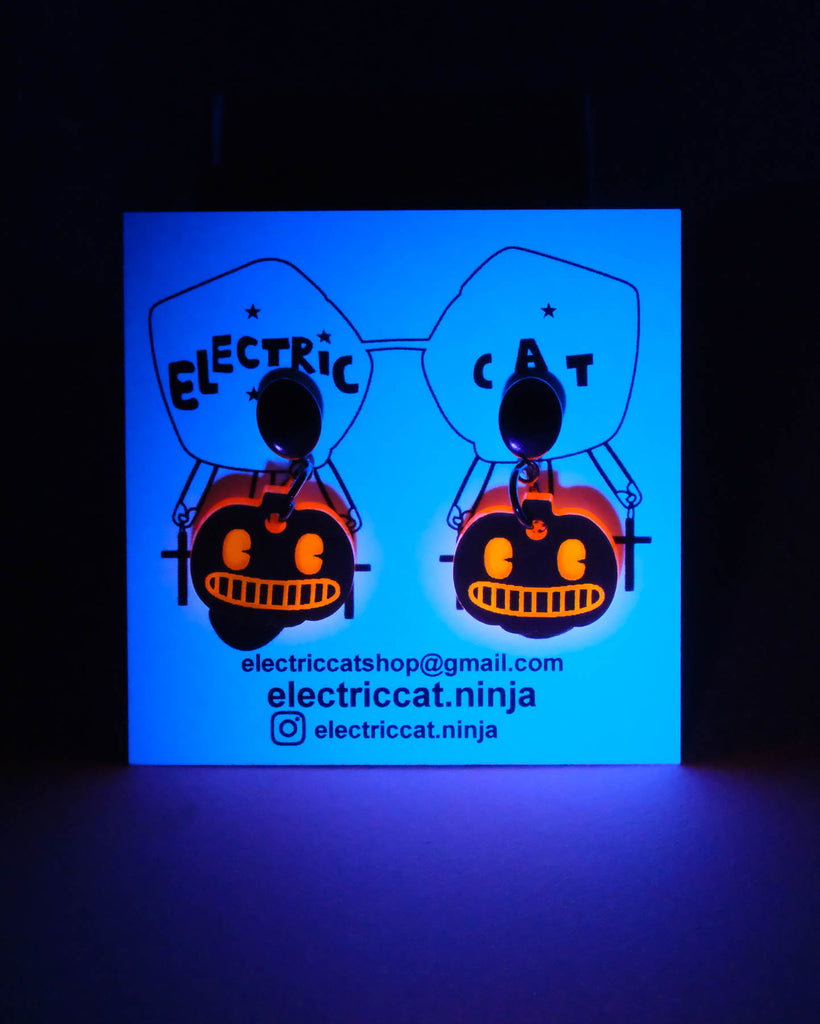 Glowing business card with pumpkin glow in the dark earrings on a black background