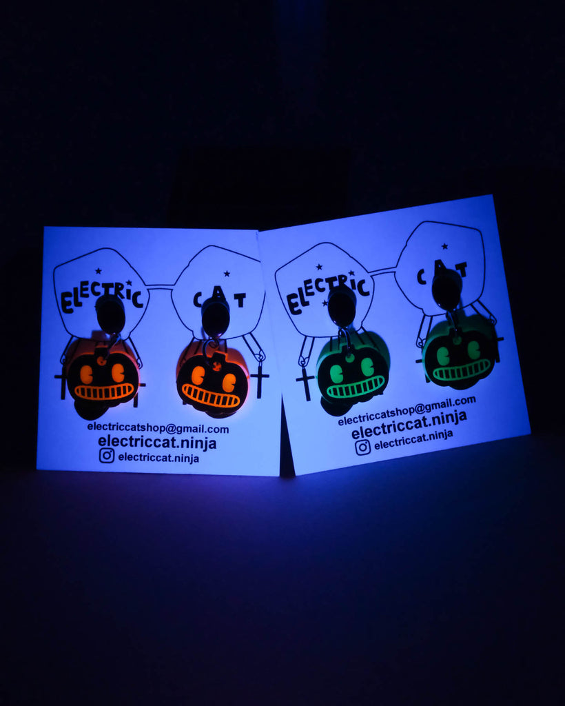 Glowing business cards with pumpkin glow in the dark earrings on a black background