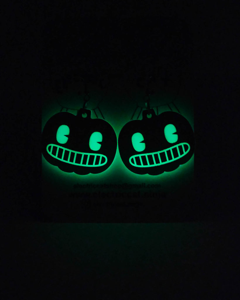 Glowing green pumpkin-shaped earrings on a black background