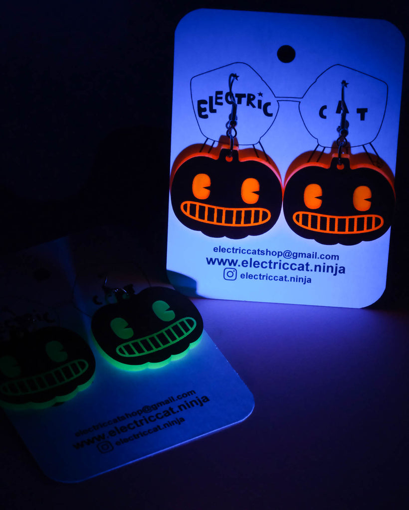 Glowing Halloween-themed earrings on a dark background with a branded card.