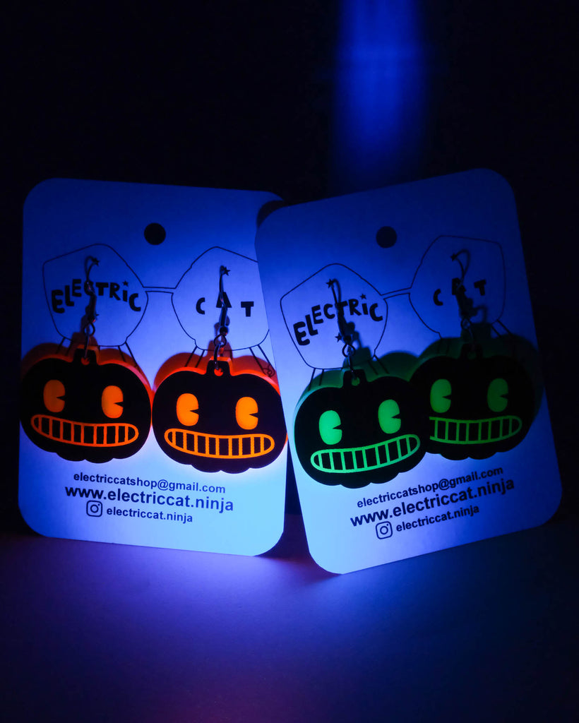 Two glowing pumpkins earrings under a blue light.