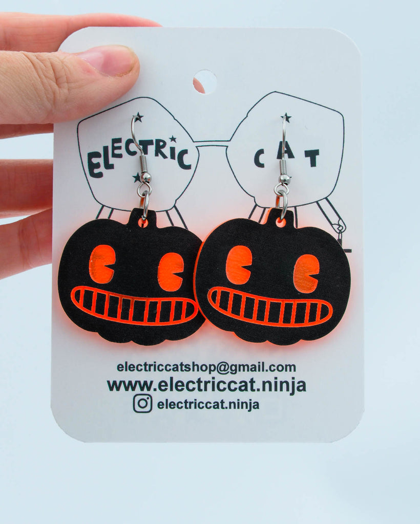 Black and orange pumpkin-shaped earrings on a 'Electric Cat' branded card.