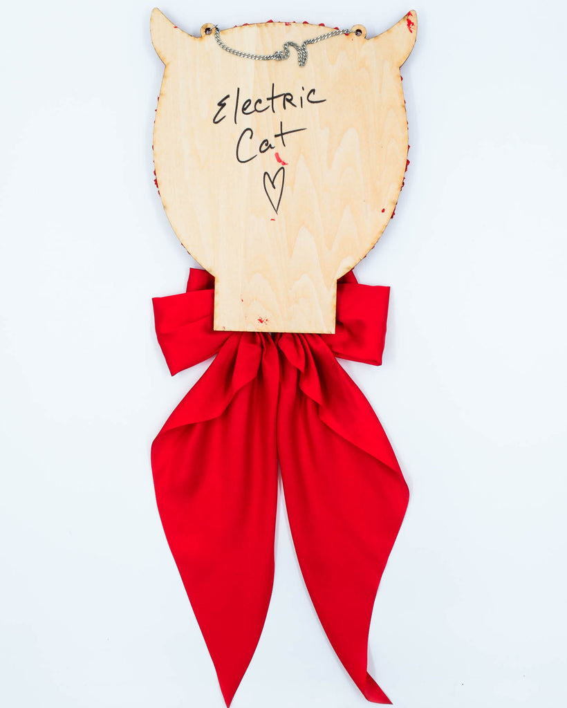 Red devil-themed mirror with sculpted frosting details, horns, and long satin ribbon bow, art by Electric Cat.