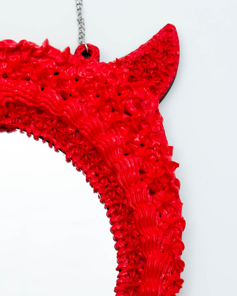 Red devil-themed mirror with sculpted frosting details, horns, and long satin ribbon bow, art by Electric Cat.