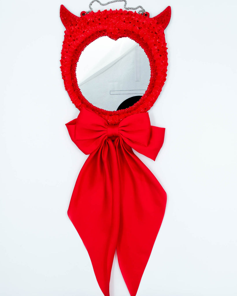 Red devil-themed mirror with sculpted frosting details, horns, and long satin ribbon bow, art by Electric Cat.