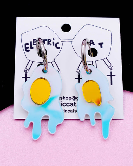 A pair of iridescent, drippy egg-shaped earrings with yellow mirror acrylic on stainless steel hoops, displayed on a white card with 'Electric Cat' branding.