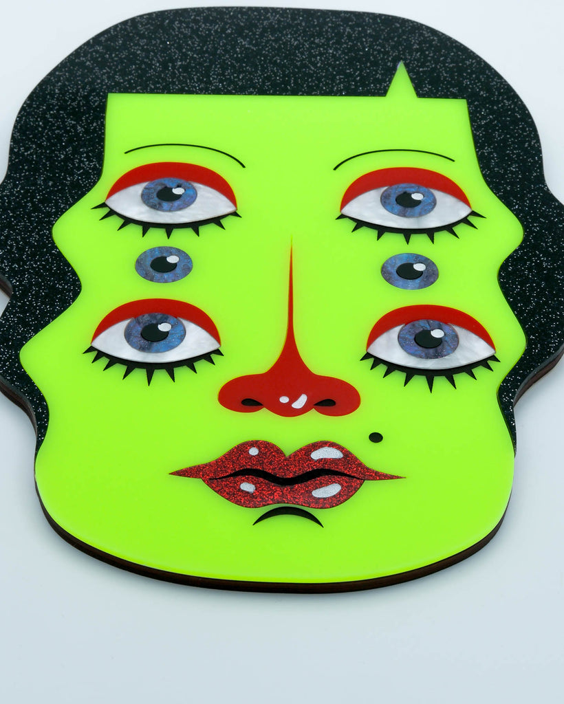 Handmade acrylic wall art featuring a neon green face with six eyes, black glitter hair, and red accents, art by Electric Cat.